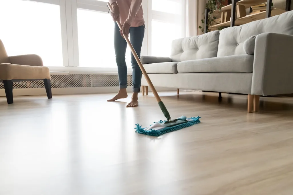 Cropped close up image of barefoot young woman in casual clothes washing wooden laminate floor using microfiber wet mop pad, doing cleaning routine